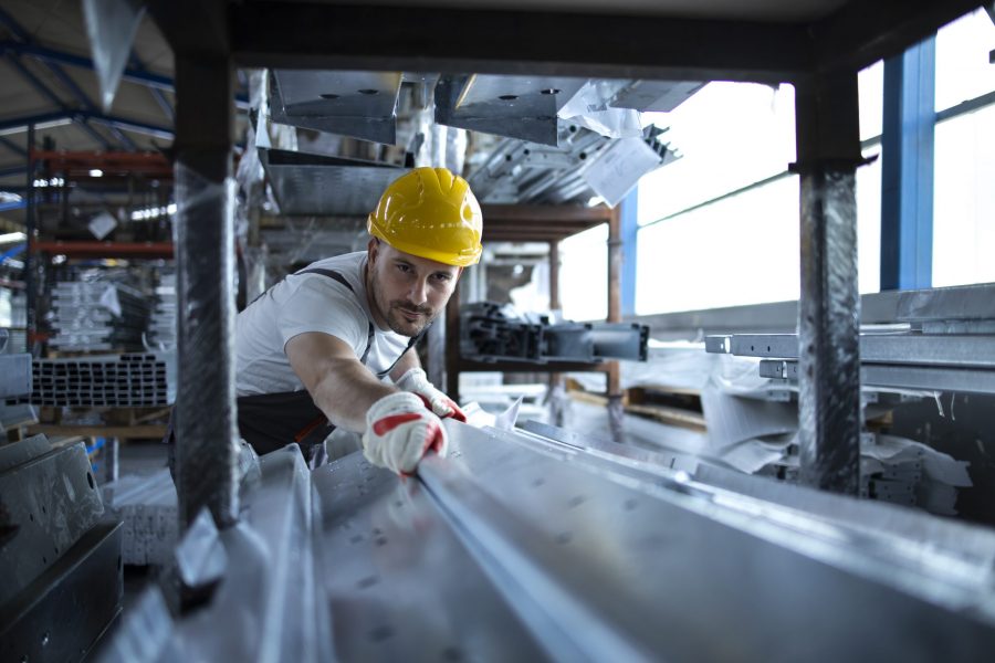 Factory worker working in warehouse handling metal material for production.